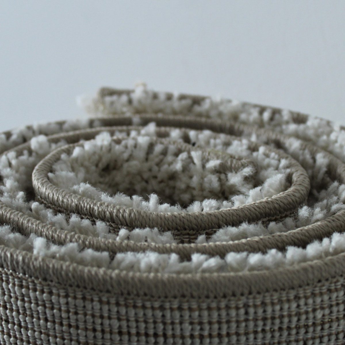 A rolled rug sits on a flat surface, showcasing textured fibers in neutral colors, suggesting softness and warmth in a simple environment.