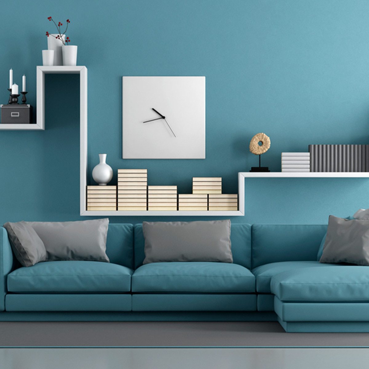A turquoise couch with throw pillows rests against a matching wall. Above, shelves display books, decorative items, and a clock, creating a modern living space.