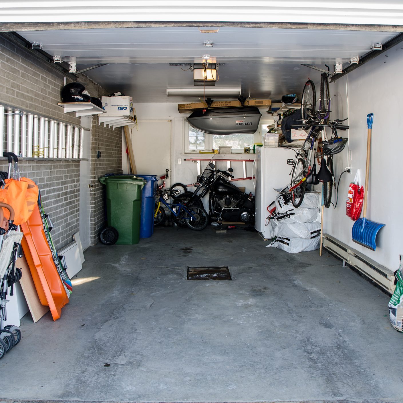 A cluttered garage contains various items, including bicycles and a motorcycle, under artificial lighting, with a concrete floor and walls partially exposed.