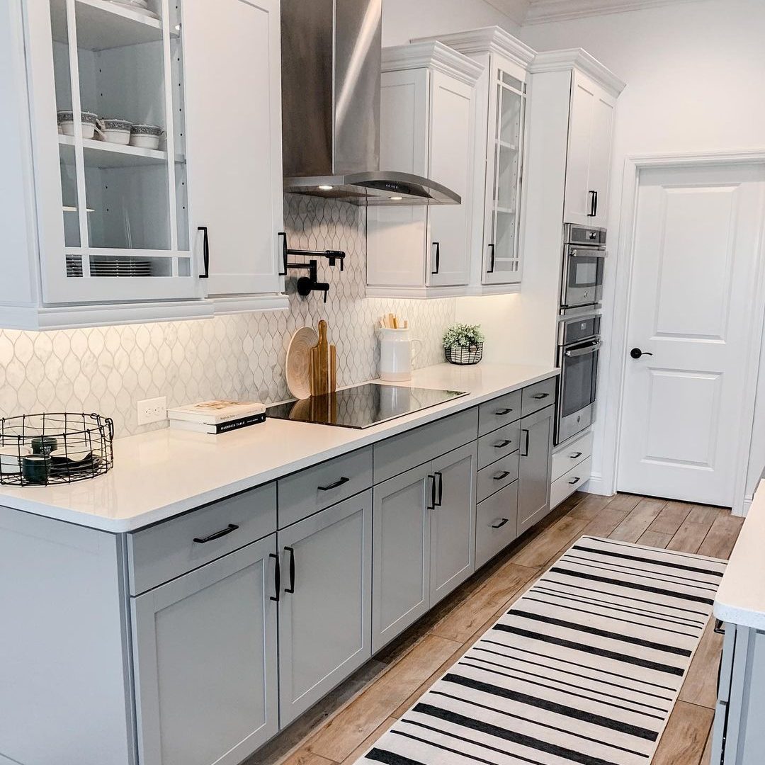 A modern kitchen features gray cabinetry and stainless steel appliances. A countertop hosts utensils; a striped rug adds warmth to the wooden floor.