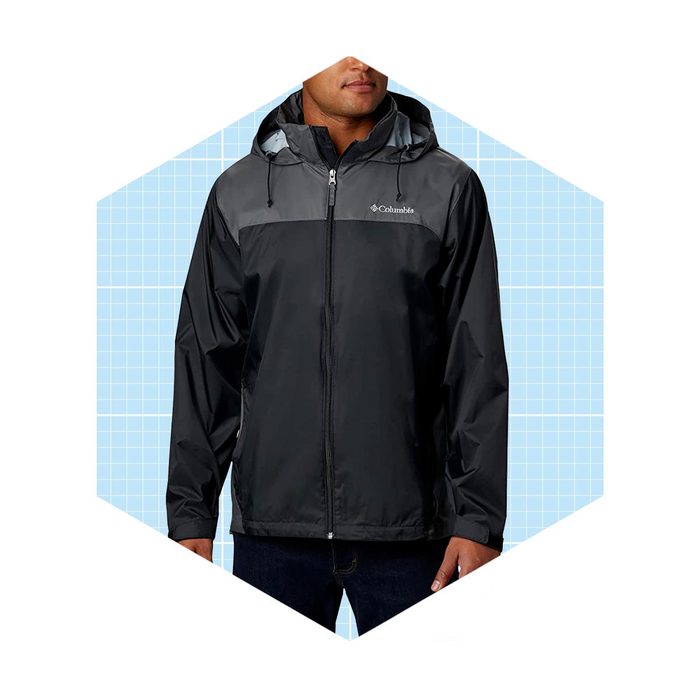 A man is wearing a black rain jacket with a gray yoke, standing against a light blue grid background.