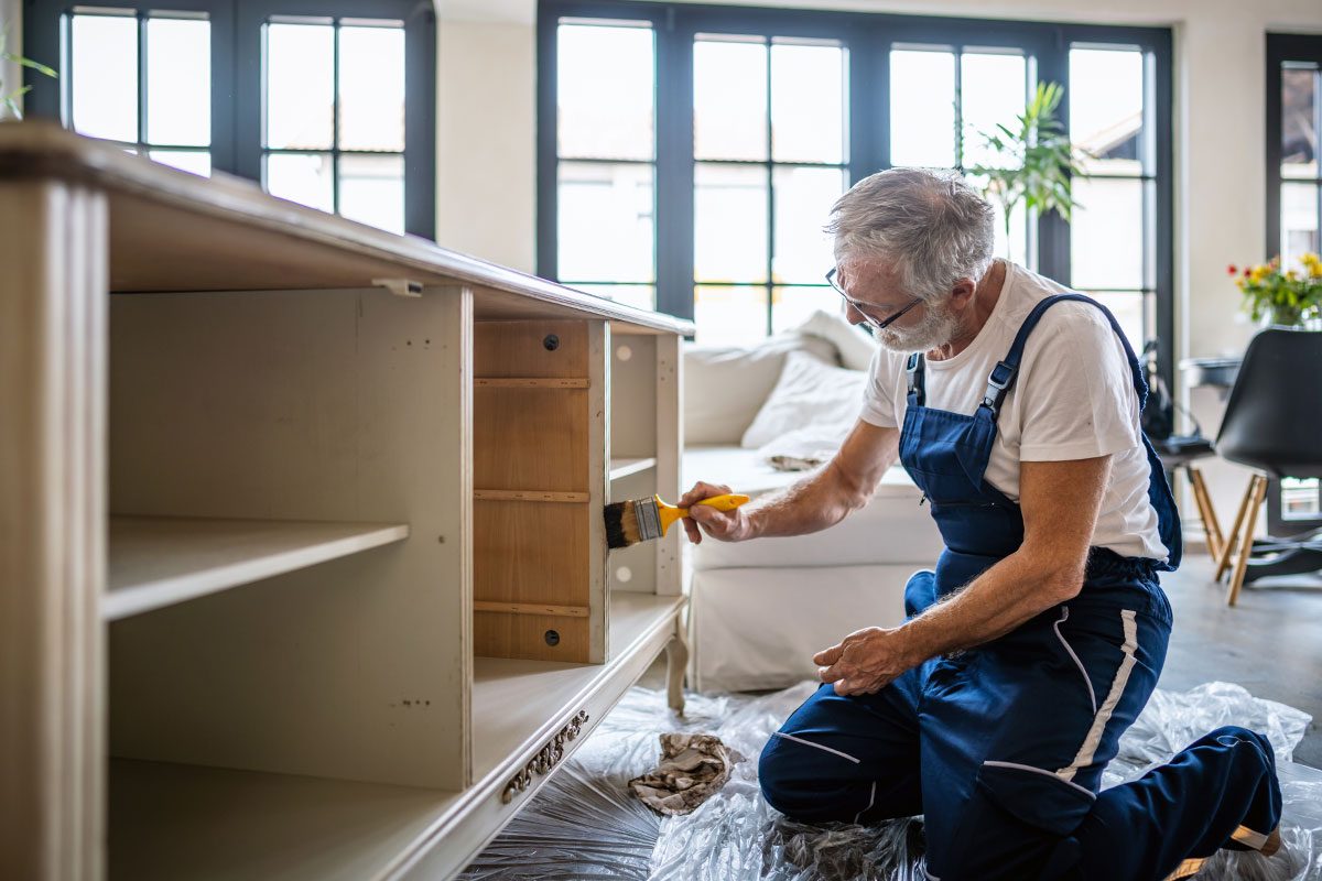 Senior man painting an old showcase in the living room