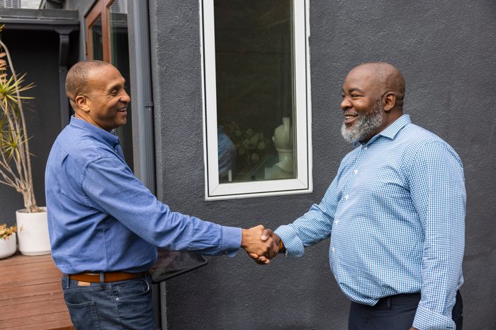 Happy mature man doing handshake with salesman while standing outside house