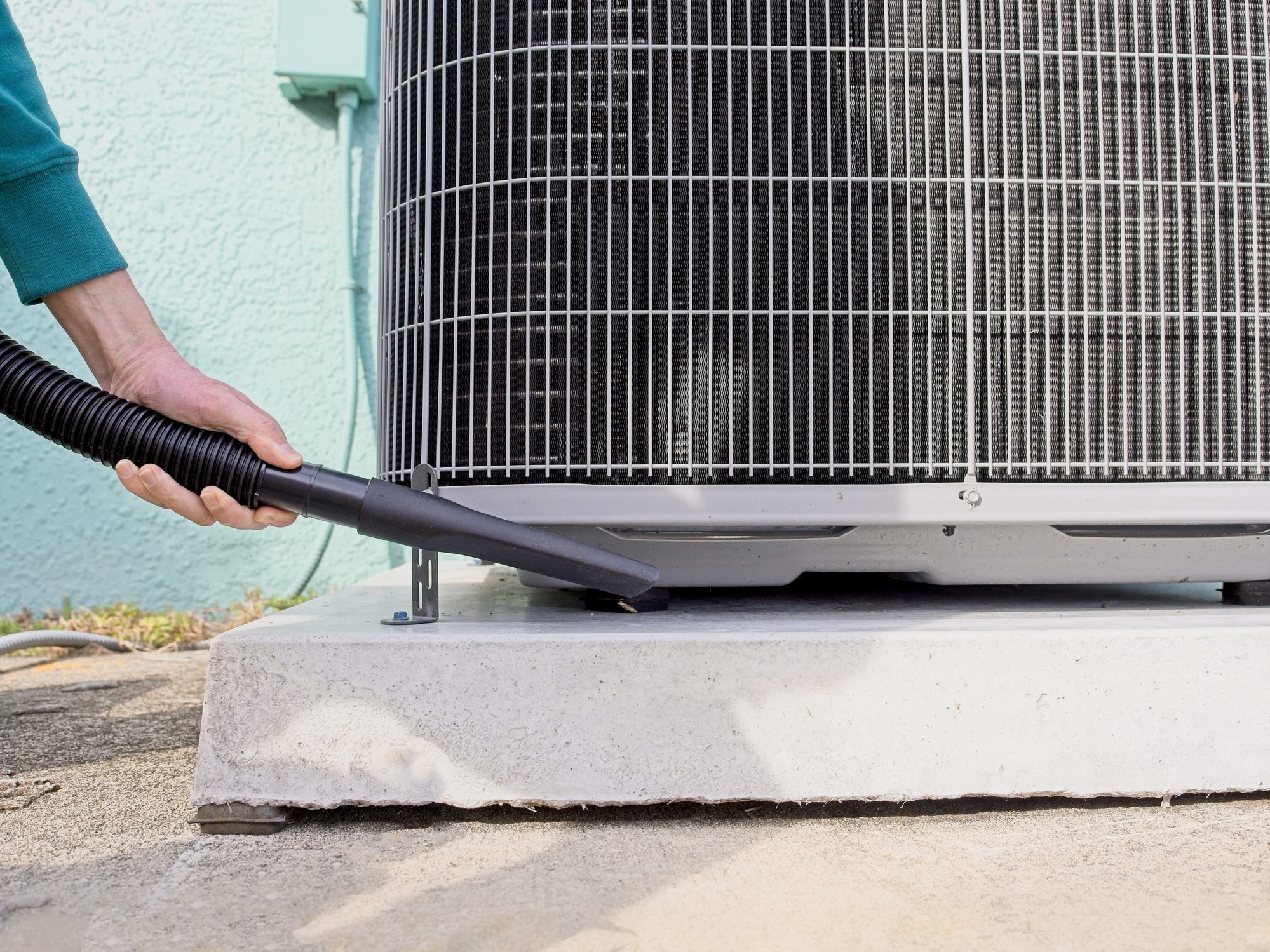 Home owner vacuums around heat pump to ensure peak efficiency for the HVAC system in Melbourne, Florida - USA