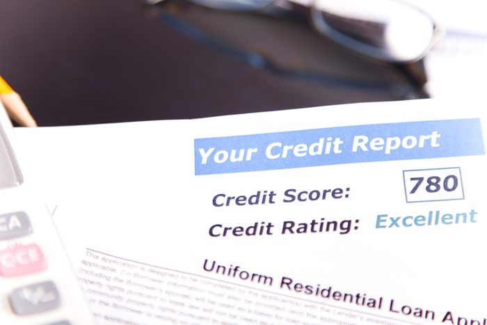 Credit report, score, loan documents, digital tablet, eyeglasses, and calculator on desk.