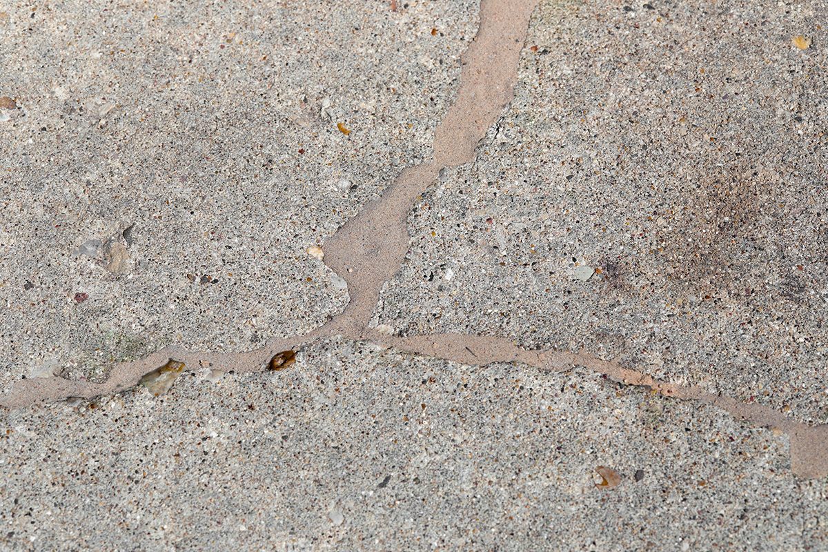 Close-up of a concrete surface with several visible cracks, some filled with a lighter material, showing signs of wear and age.